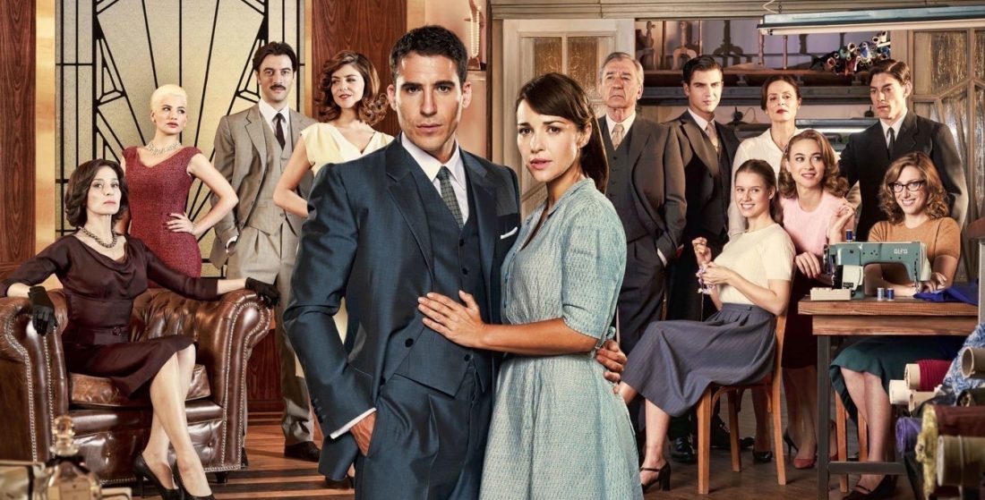 Velvet TV series cast, standing together in elegant period costumes inside a fashion house.