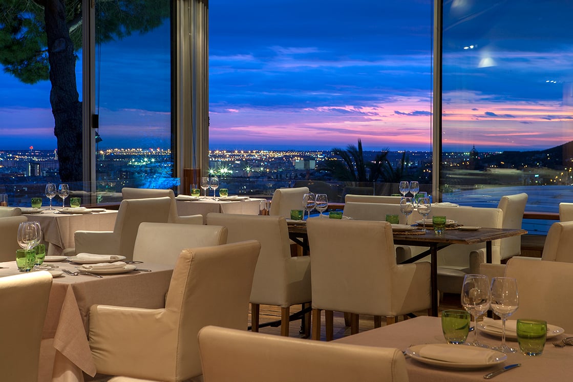 Dining area of Mirabé Restaurant in Barcelona with a panoramic view of the city during sunset.