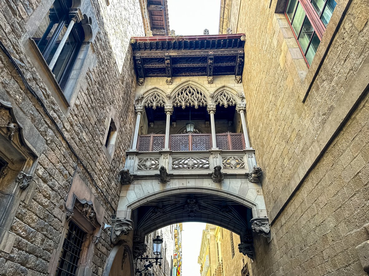 Detailed view of the Pont del Bisbe, a neo-Gothic bridge in the Gothic Quarter of Barcelona, connecting historic stone buildings.