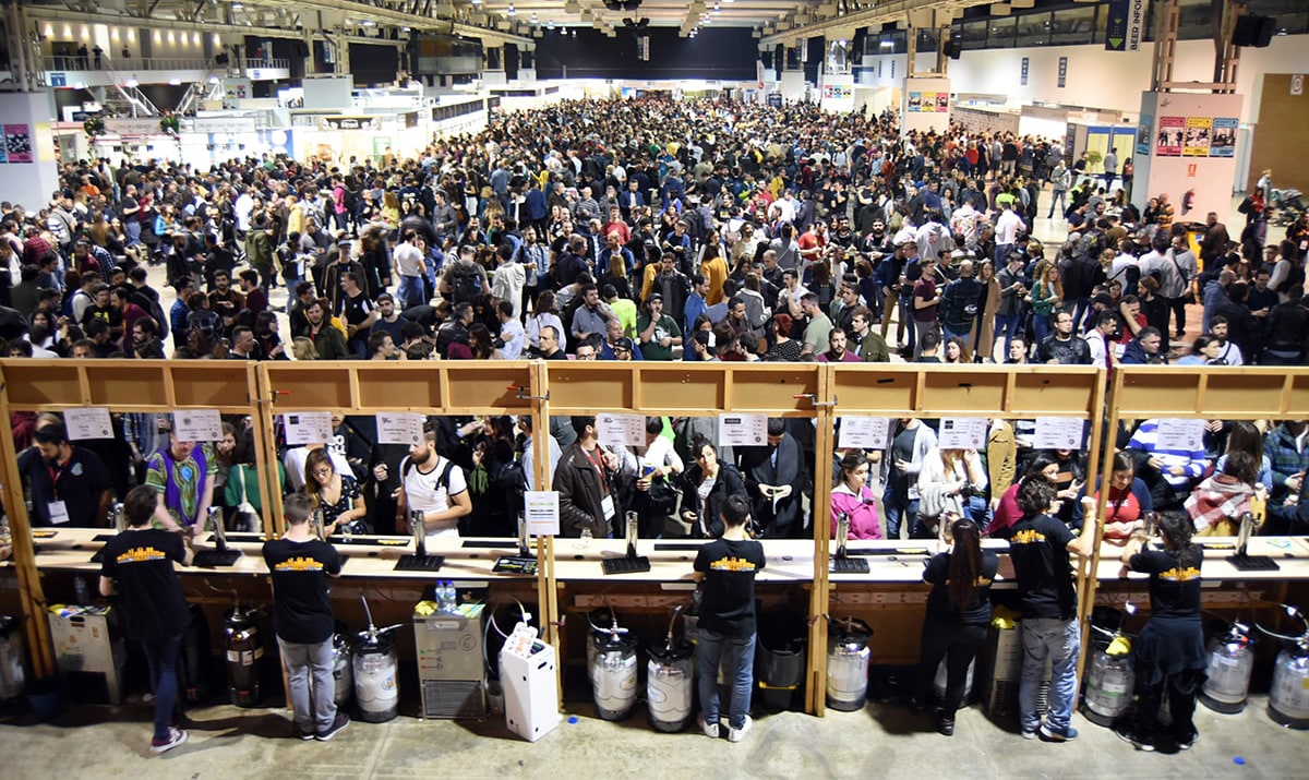 A large crowd attending the Barcelona Beer Festival at Fira de Barcelona, with people gathering around a bar serving various craft beers.