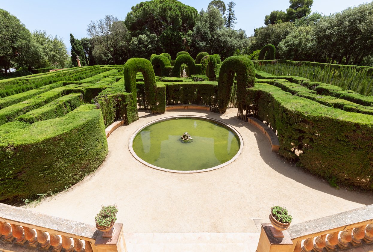 The intricate hedge maze at Parc del Laberint d'Horta in Barcelona, surrounded by lush greenery with a central circular fountain, creating a serene and historic garden landscape.