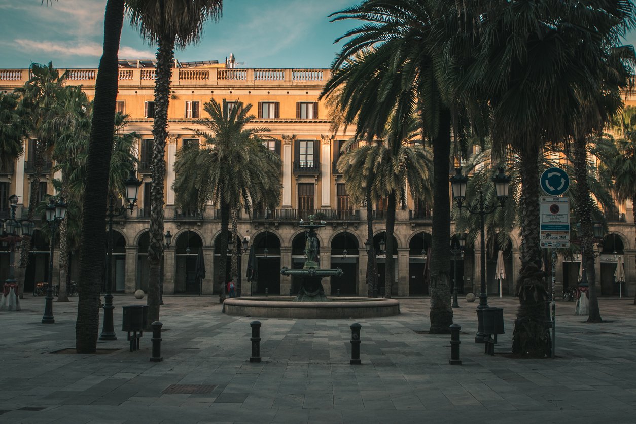 Empty and serene view of Plaça Reial in Barcelona during sunset, with palm trees and historic buildings, capturing a rare moment of quiet in this usually bustling square.