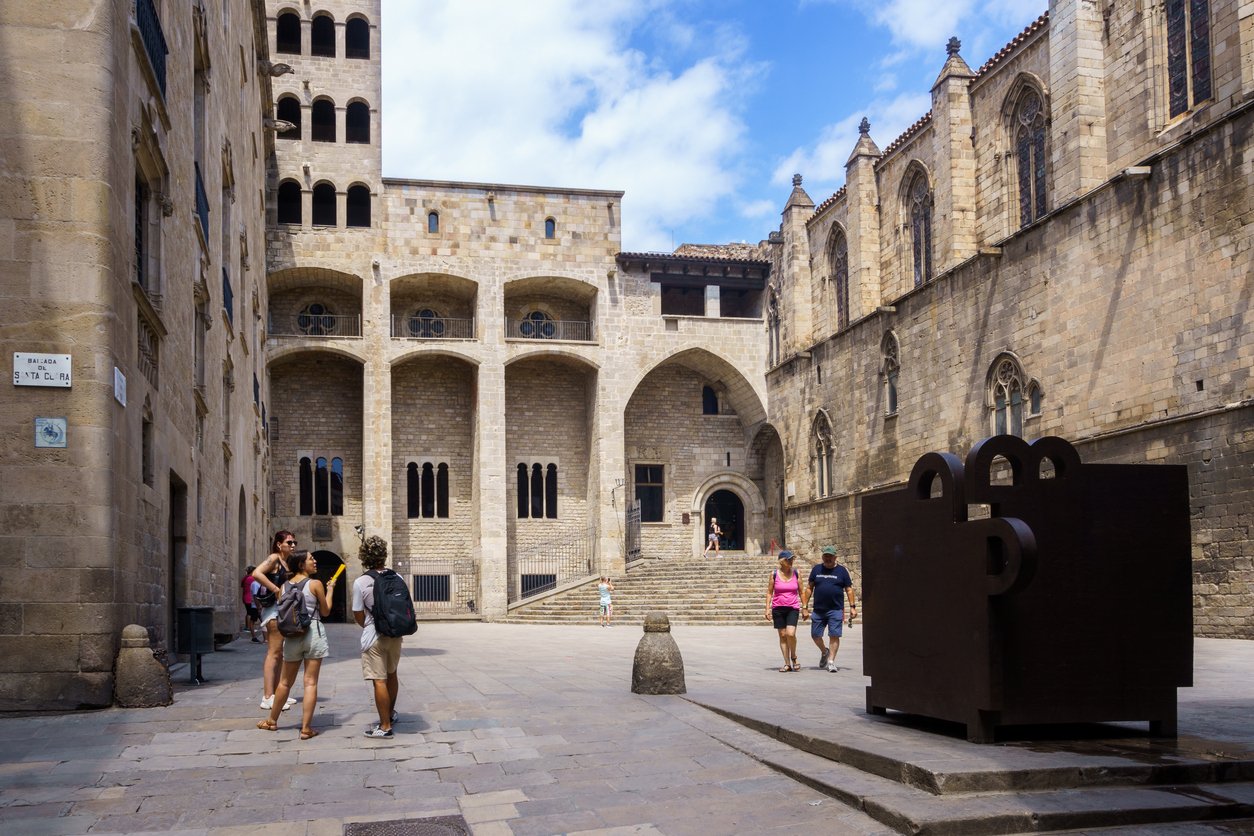 View of Plaça del Rei in Barcelona's Gothic Quarter, showcasing historic stone buildings, arches, and tourists exploring the square.