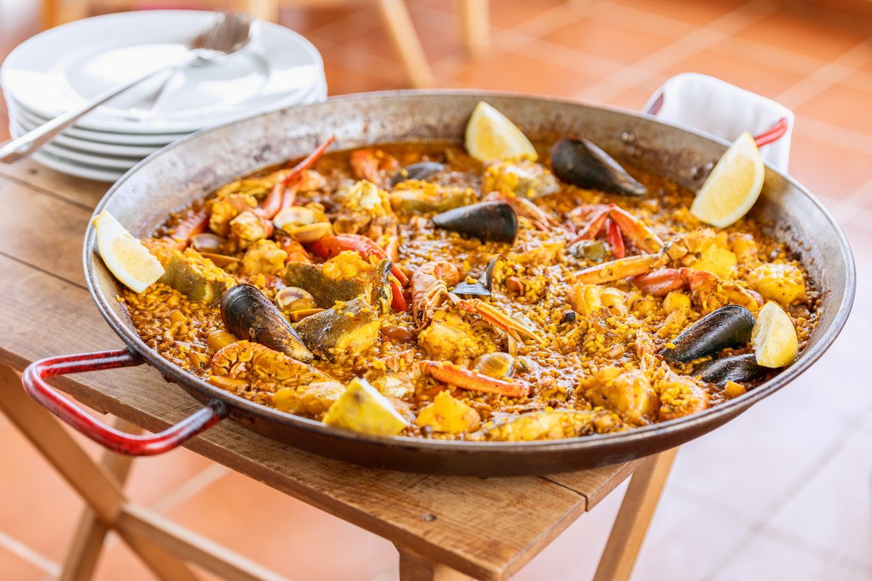 Seafood paella with mussels, shrimp, and lemon wedges served in a large pan.