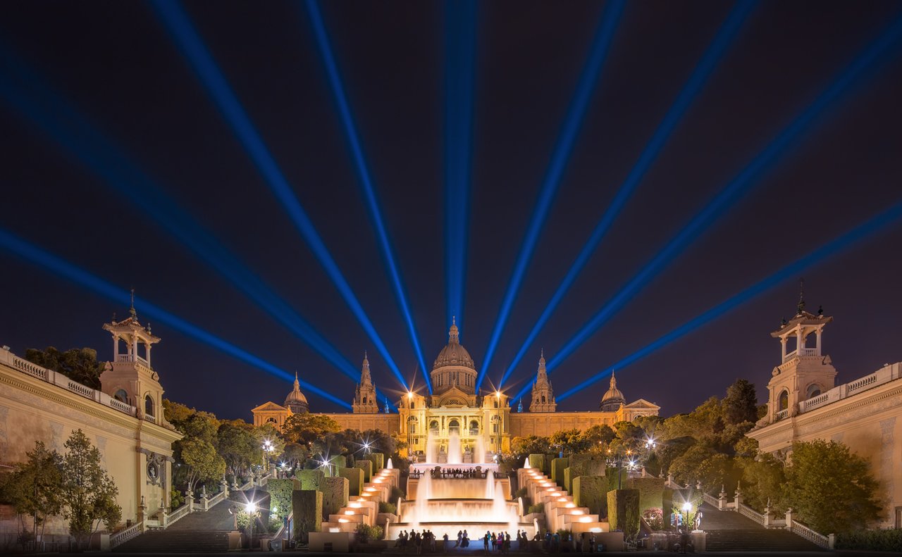 Night view of Montjuïc's Magic Fountain with stunning blue light beams illuminating the Museu Nacional d'Art de Catalunya in Barcelona.
