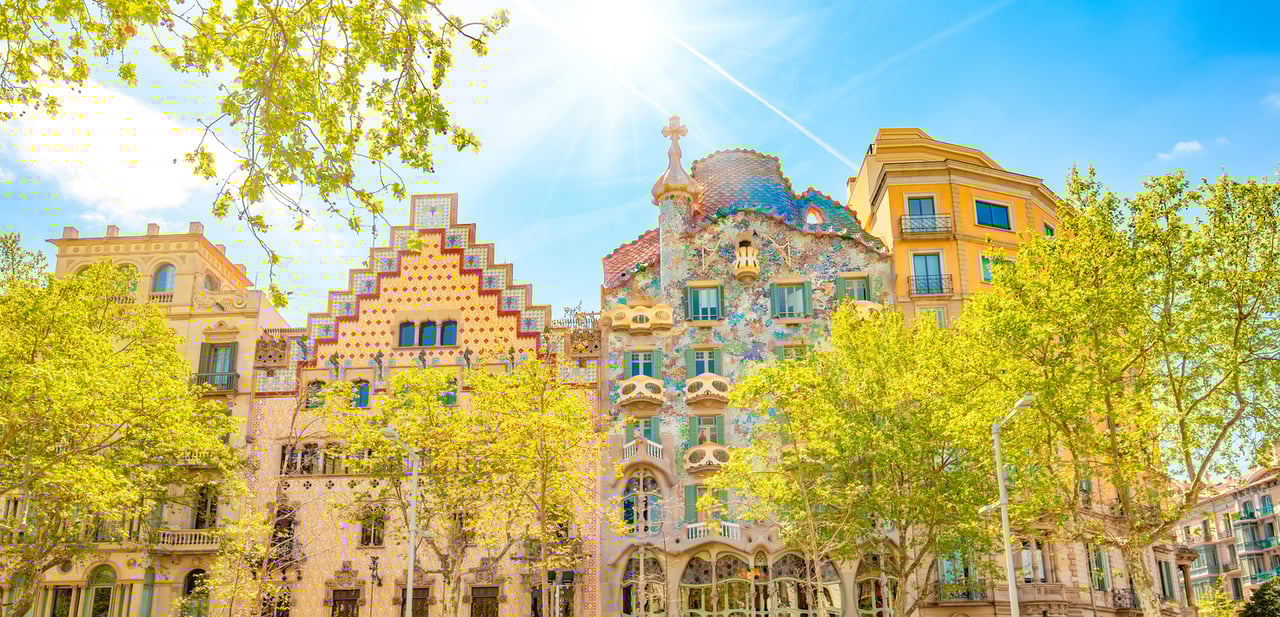 Casa Batlló and surrounding modernist buildings in the vibrant Eixample neighborhood of Barcelona, showcasing Gaudí's colorful architecture amidst tree-lined streets and bright sunshine, reflecting the area's rich cultural and architectural heritage.