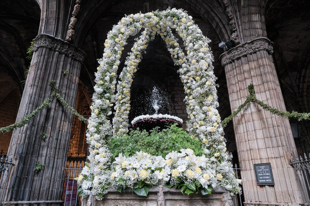 A beautifully decorated fountain with floral arrangements as part of the traditional "Ou com Balla" celebration during Corpus Christi in Barcelona, where an egg is balanced on a stream of water.