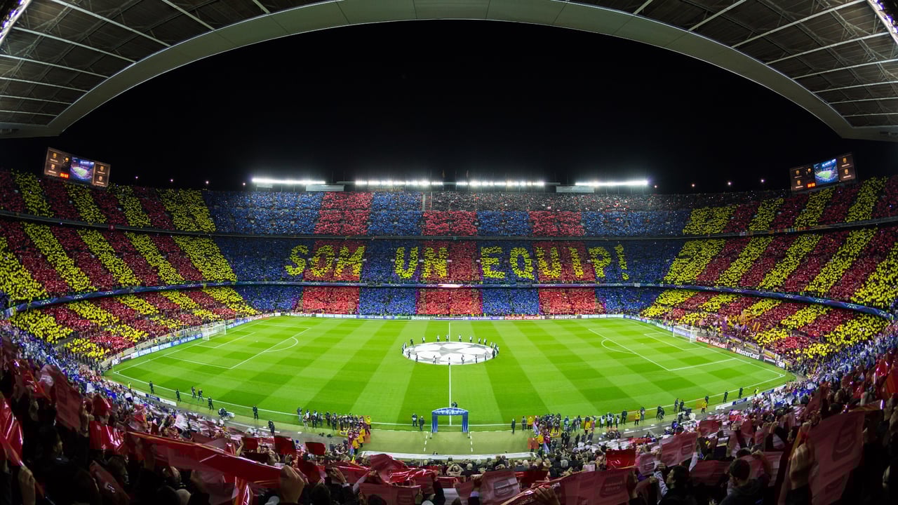 Camp Nou stadium in Barcelona during a UEFA Champions League match, with fans creating a colorful mosaic in the stands.