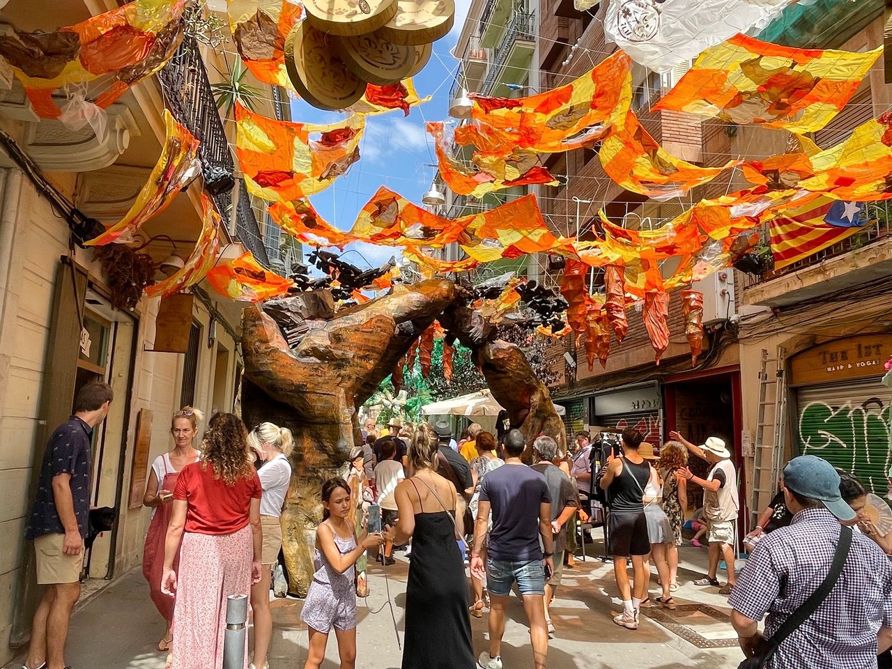 Colorful street decorations at the Festa Major de Gràcia in Barcelona, featuring vibrant banners, artistic sculptures, and a lively crowd of visitors.