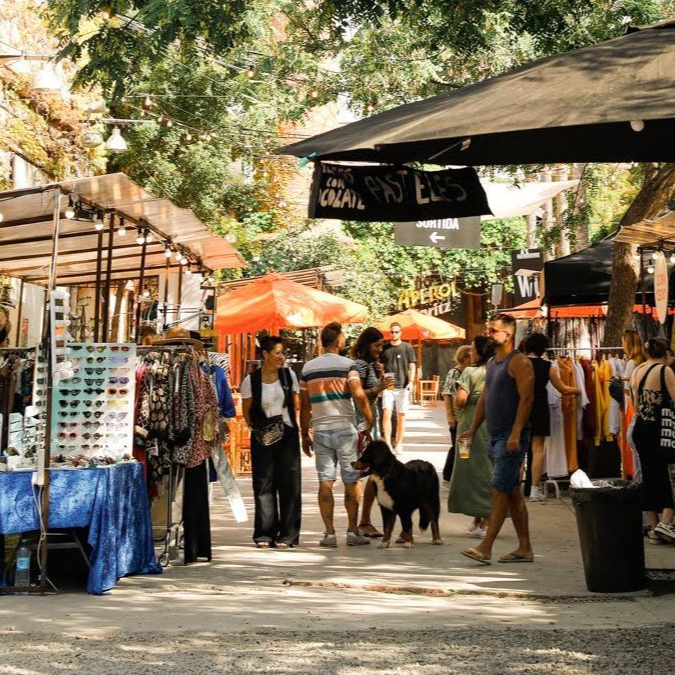 Outdoor scene at the Palo Alto Market in Barcelona, with various stalls selling accessories and fashion items under the shade of trees.