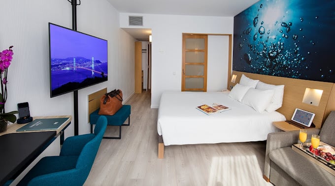Stylish room at Novotel Barcelona Cornella with a comfortable double bed, bright blue accent wall art, mounted TV, work desk, seating area, and contemporary decor offering a cozy yet modern atmosphere.