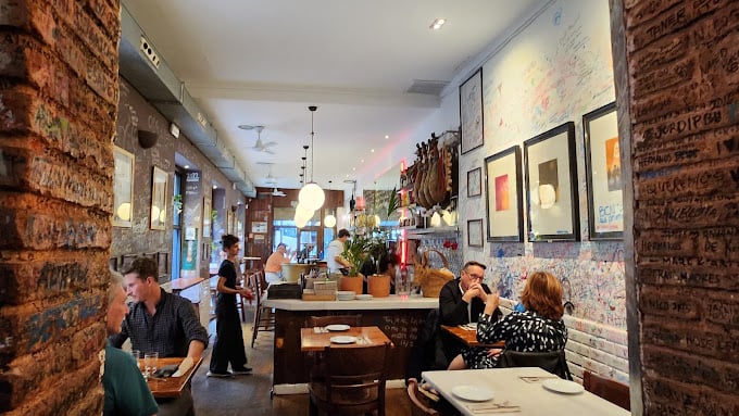 Interior of Bar Mut, a cozy and stylish restaurant in Barcelona, featuring brick walls, a bar, and patrons enjoying their meals in a warmly lit atmosphere.