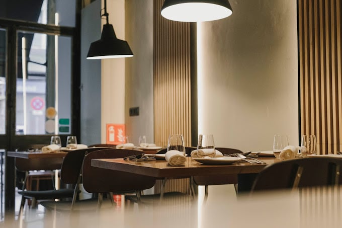 Minimalist interior of Maleducat in Barcelona, featuring wooden tables set for dining, modern pendant lighting, and a warm, inviting ambiance.