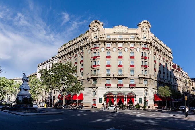 Majestic historic building with a classical facade, vibrant red accents, and a prominent corner location, home to El Palace Barcelona.