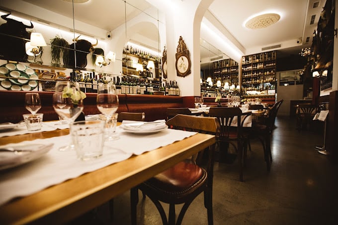 Interior of Bar Cañete, featuring elegantly set tables with glasses and plates, warm lighting, and shelves lined with bottles in a cozy, sophisticated atmosphere.