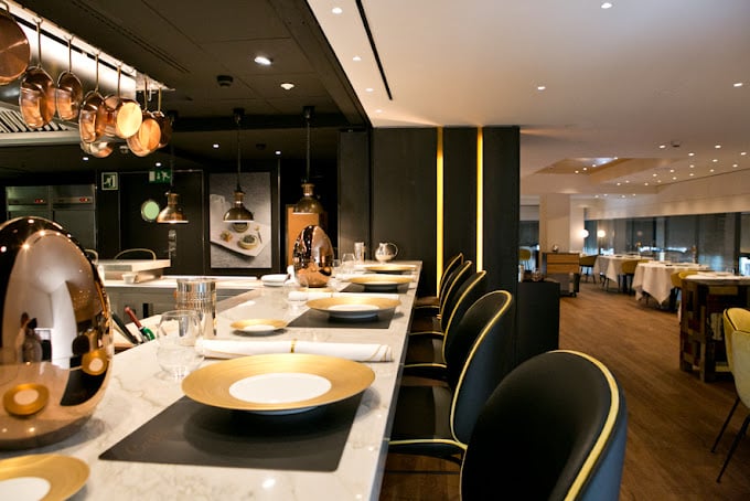 Modern interior of Caelis restaurant in Barcelona, featuring elegant counter seating with gold accents and an open kitchen atmosphere.