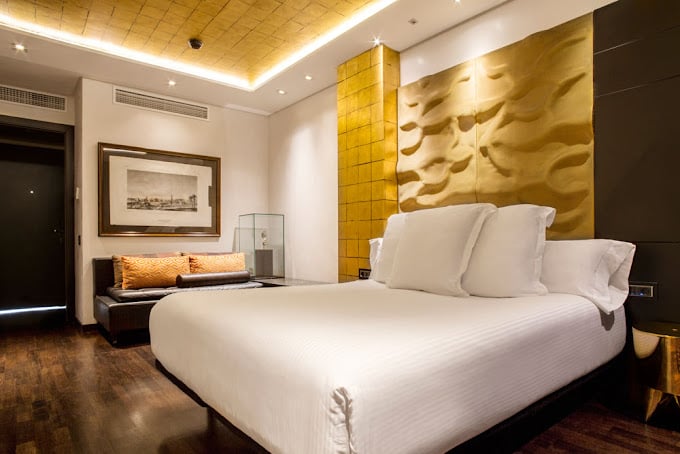 Sophisticated hotel room with golden decor accents, plush bedding, and modern art features at Hotel Claris in Barcelona.