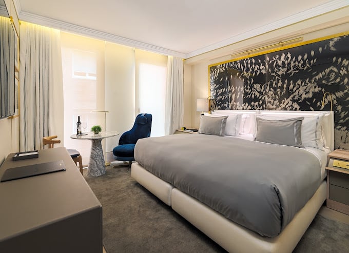 Contemporary hotel room with a stylish gray and gold theme, offering luxurious bedding and a relaxing atmosphere at The One Barcelona.