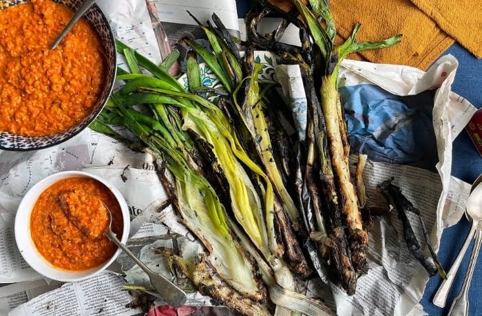 Grilled calçots served with romesco sauce, a traditional Catalan dish, laid out on newspaper.