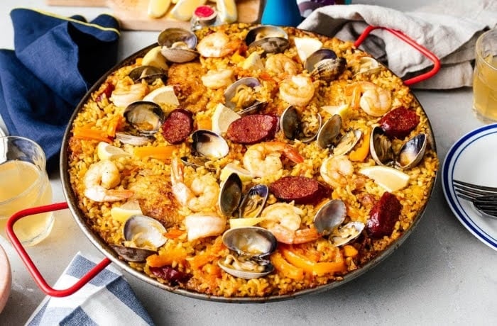 Mixed paella featuring a variety of seafood, chorizo, and vegetables, served in a traditional paella pan with lemon wedges.