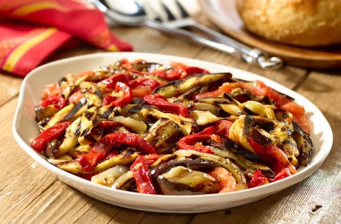 Escalivada, a traditional Catalan dish of roasted vegetables, including eggplant and red peppers, served on a white plate.