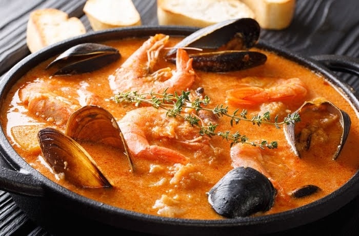 Suquet de Peix, a traditional Catalan seafood stew with shrimp, mussels, and fish in a tomato-based broth, served in a black pot.
