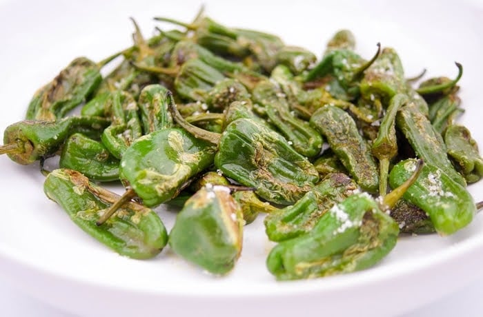 Pimientos de Padrón, a dish of Spanish fried green peppers, lightly salted and served on a white plate.