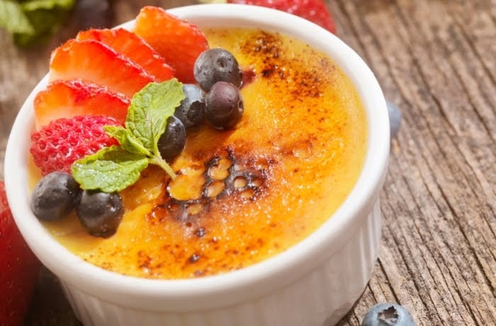 Crema Catalana, a traditional Spanish custard dessert with a caramelized sugar topping, garnished with fresh strawberries and blueberries.