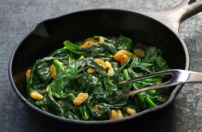 Spinach sautéed with raisins and pine nuts, a traditional Catalan dish, served in a black skillet.
