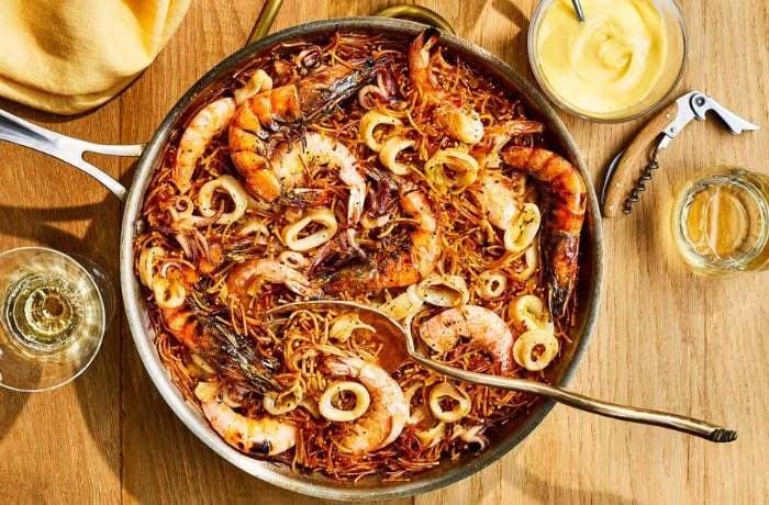 Fideuà, a traditional Catalan dish made with short noodles, shrimp, and calamari, served in a pan with aioli on the side.