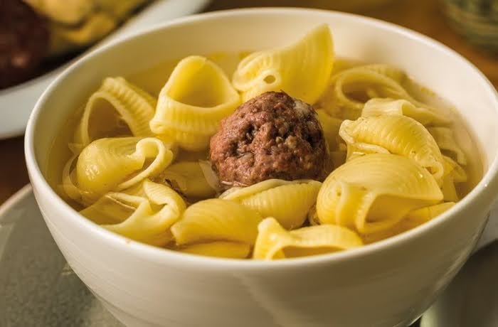 Bowl of Escudella, a traditional Catalan soup featuring pasta shells and a large meatball in a savory broth.