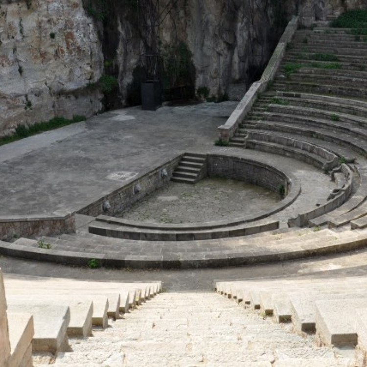 View of the Teatre Grec in Barcelona, an open-air amphitheater with stone seating and a central stage set against a rocky background