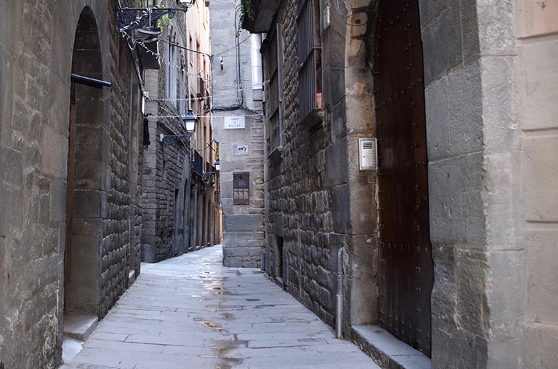 Narrow street in El Call, the historic Jewish Quarter of Barcelona, with stone buildings and medieval architecture.