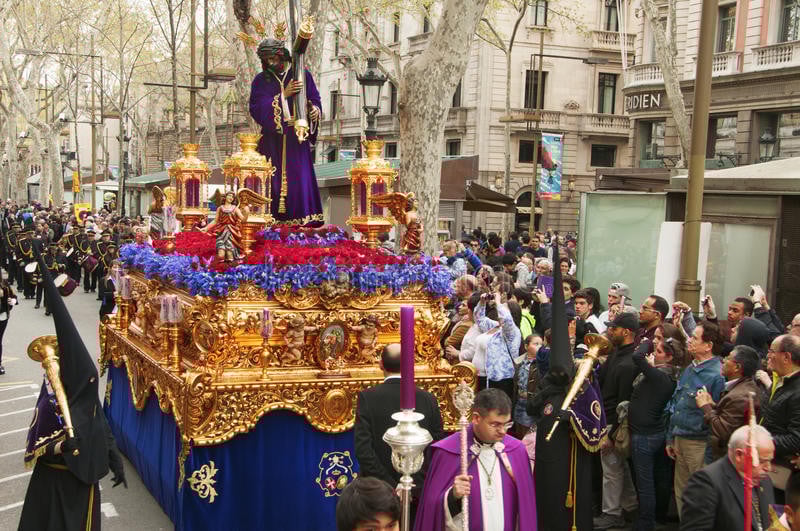Semana Santa procession on La Rambla in Barcelona with religious statues and floats, surrounded by a large crowd of onlookers.