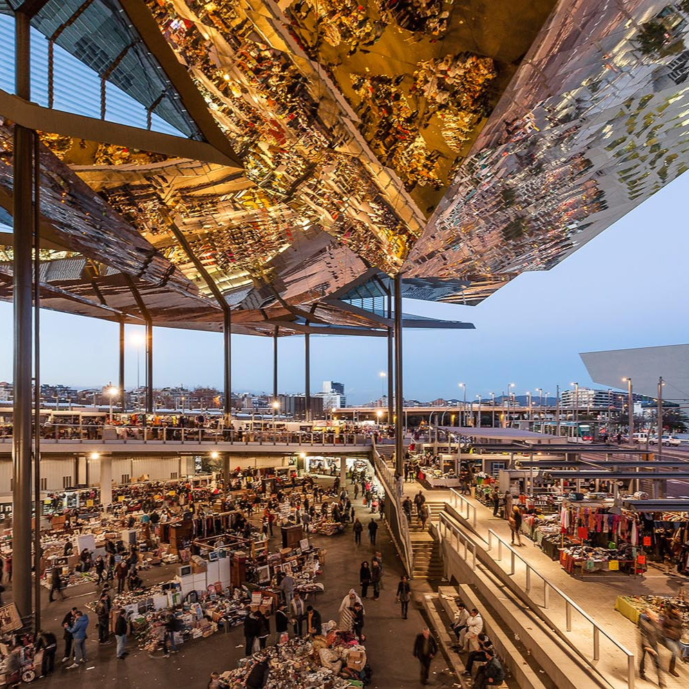 Evening view of Els Encants Market in Barcelona, with the striking mirrored ceiling reflecting the bustling stalls and shoppers below.