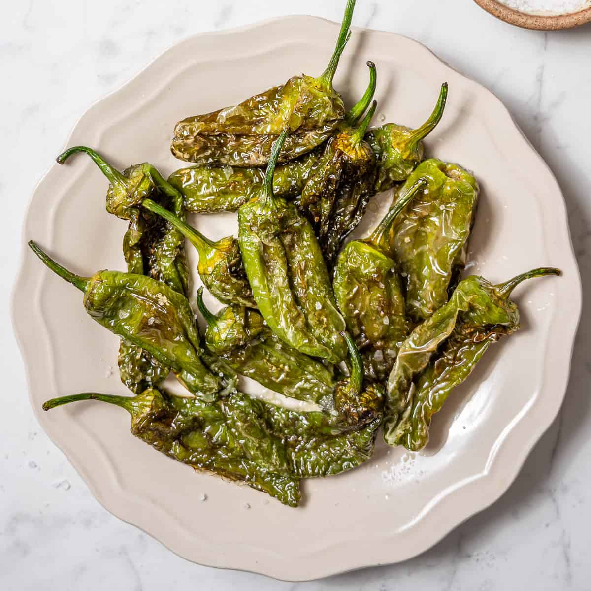 Plate of roasted Pimientos de Padrón with sea salt on a white dish.