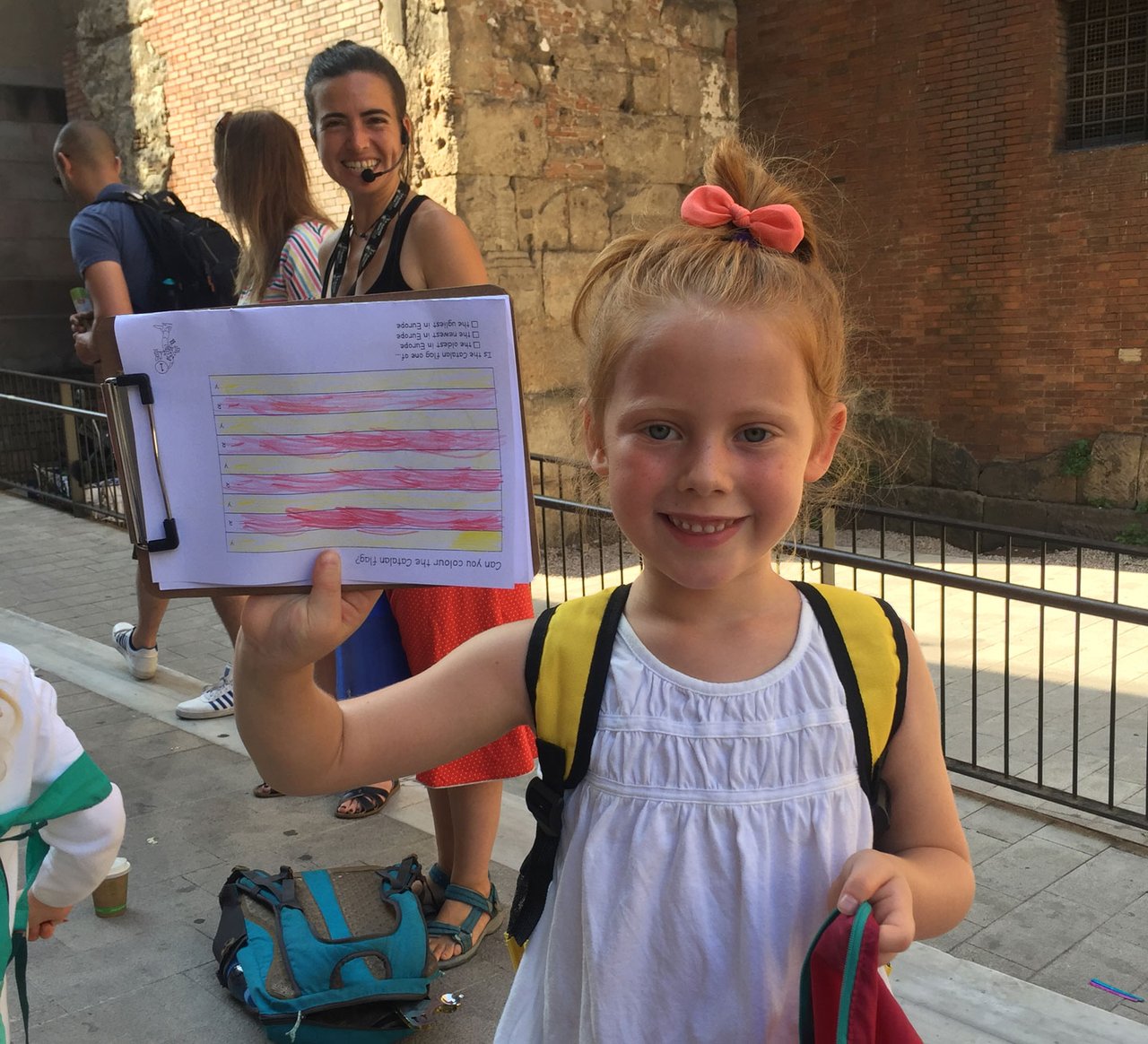 Child holding a completed coloring activity during a guided tour in Barcelona, smiling with other participants in the background.