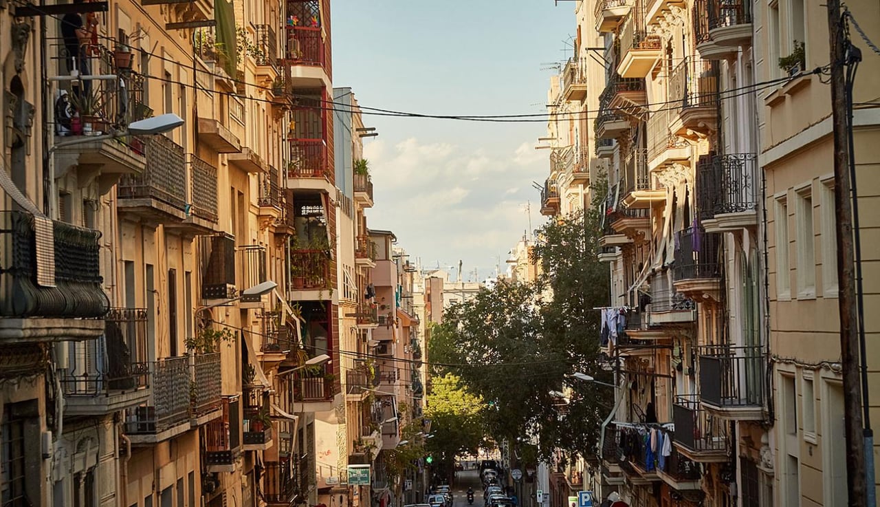 A street in Barcelona illuminated by the warm glow of sunset, with buildings on either side featuring balconies and greenery, creating a peaceful urban scene.