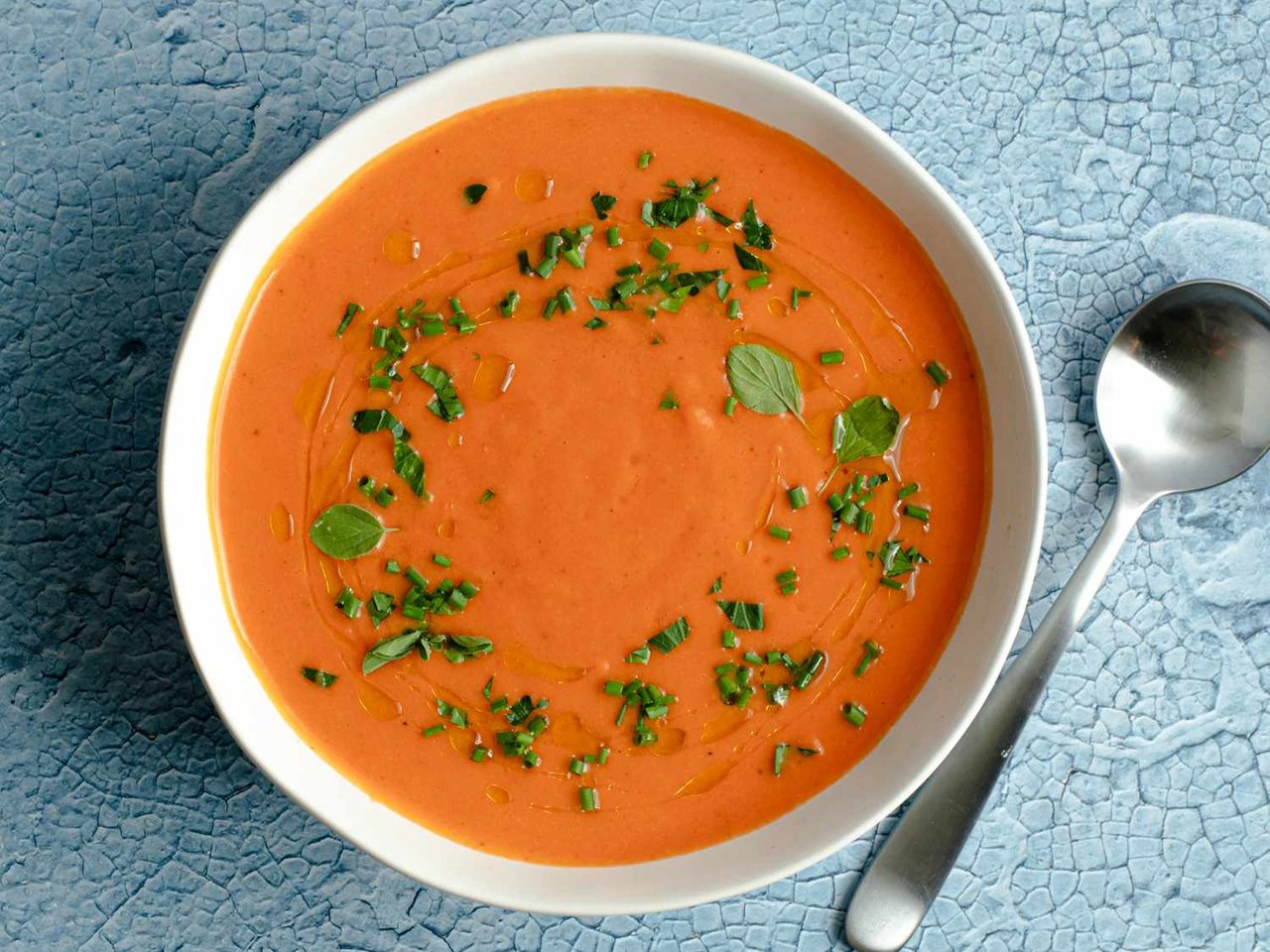 Classic gazpacho soup served in a white bowl, garnished with herbs and olive oil.