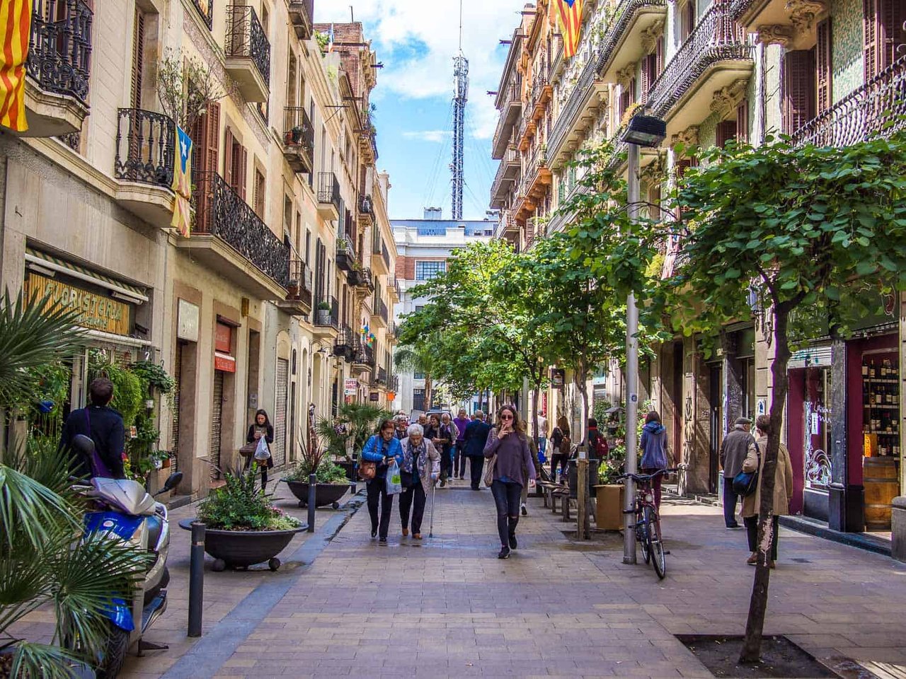 Pedestrian street in Barcelona with trees, shops, and people walking on a sunny day.