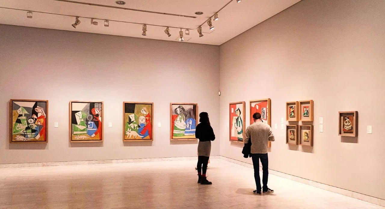 Visitors viewing paintings in an art gallery, featuring modern artwork on the walls.
