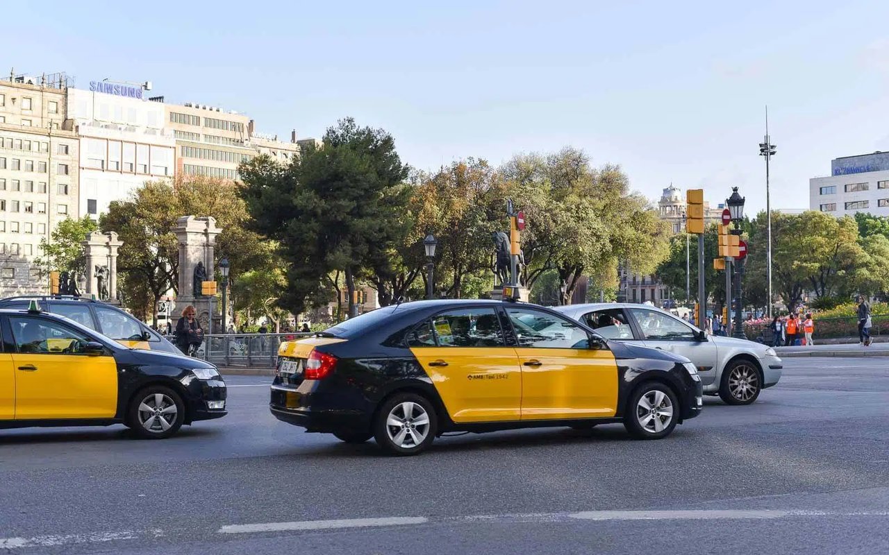 Yellow and black taxis driving through a busy street in the center of Barcelona on a sunny day.