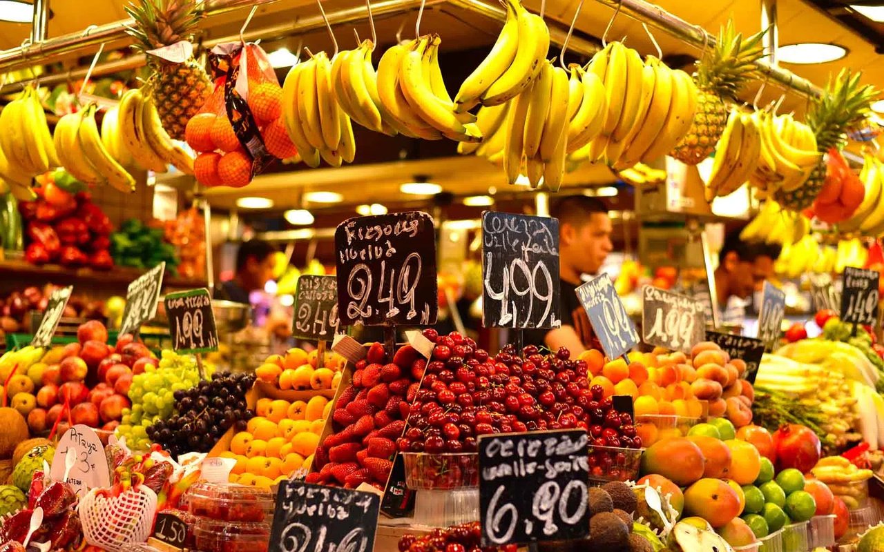 Colorful fruit and produce market stall at La Boqueria in Barcelona, with fresh bananas, cherries, and more.