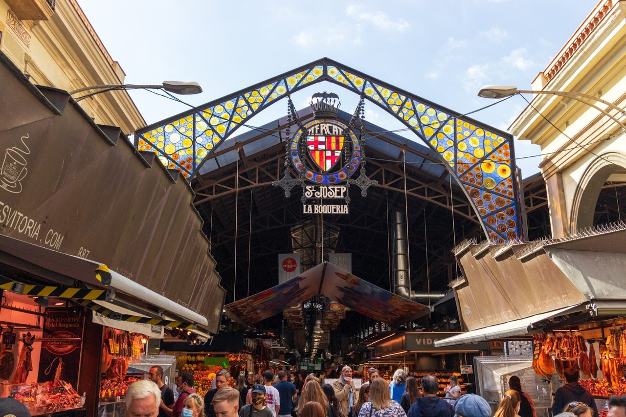 Entrance of La Boqueria Market in Barcelona with colorful stained-glass roof and crowded stalls.