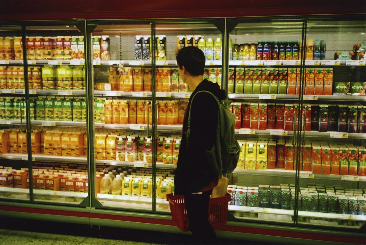 Shopper in a supermarket standing in front of a refrigerated section filled with various juice cartons.