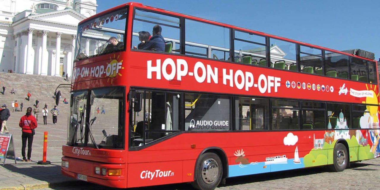 A red hop-on hop-off tour bus in front of a historic building in Barcelona, offering city tours.