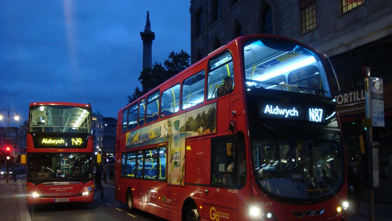 Double-decker buses driving on a street at night.
