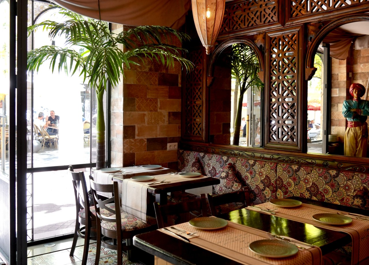Arabic-themed interior of Restaurant Aladdin in Barcelona, featuring traditional patterned cushions, wooden lattice decor, and warm ambient lighting, creating an inviting dining atmosphere.