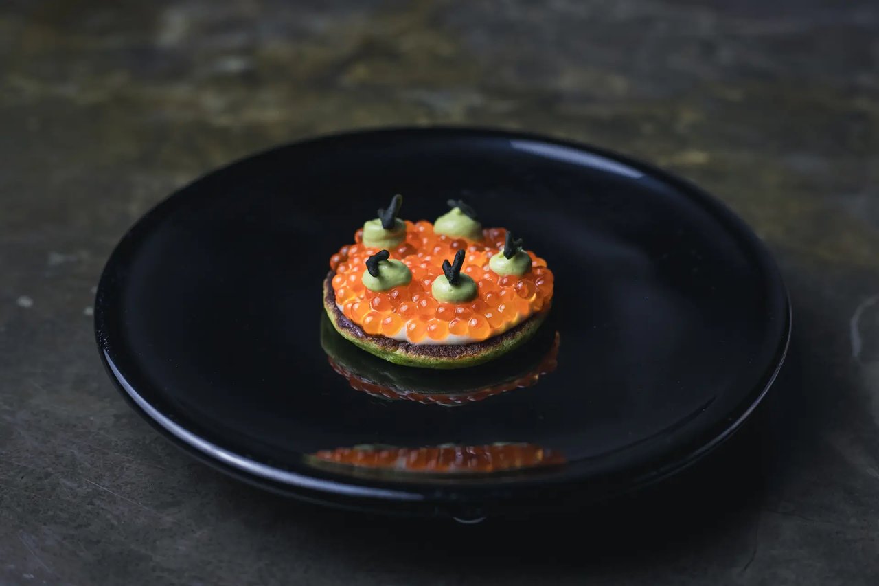 A gourmet dish with salmon roe and green sauce at Besta, Barcelona, on a black plate.