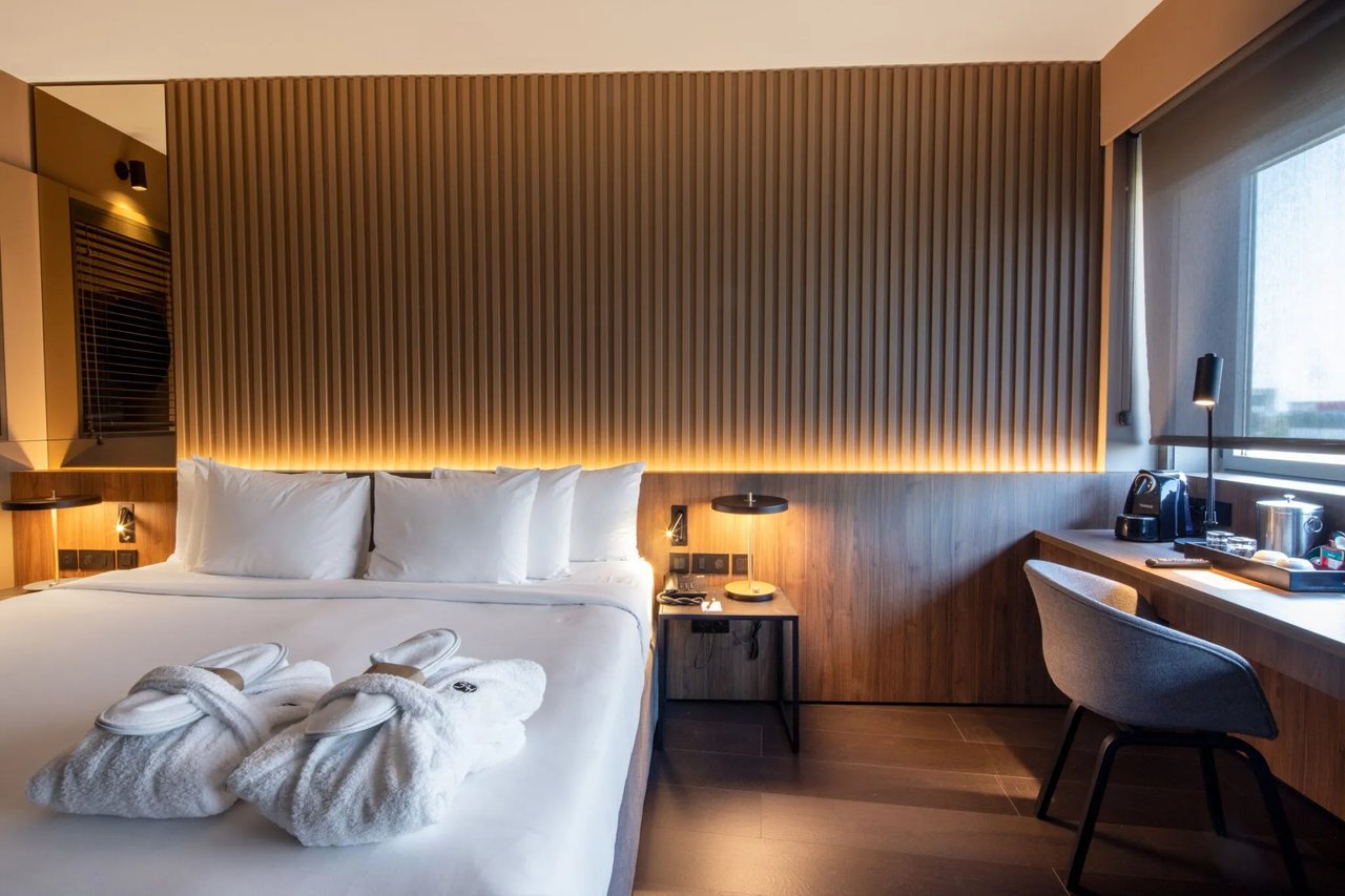Modern interior of an elite room at a Barcelona airport hotel, featuring a sleek design with a comfortable bed, soft lighting, wooden accents, and a workspace equipped with a coffee machine.